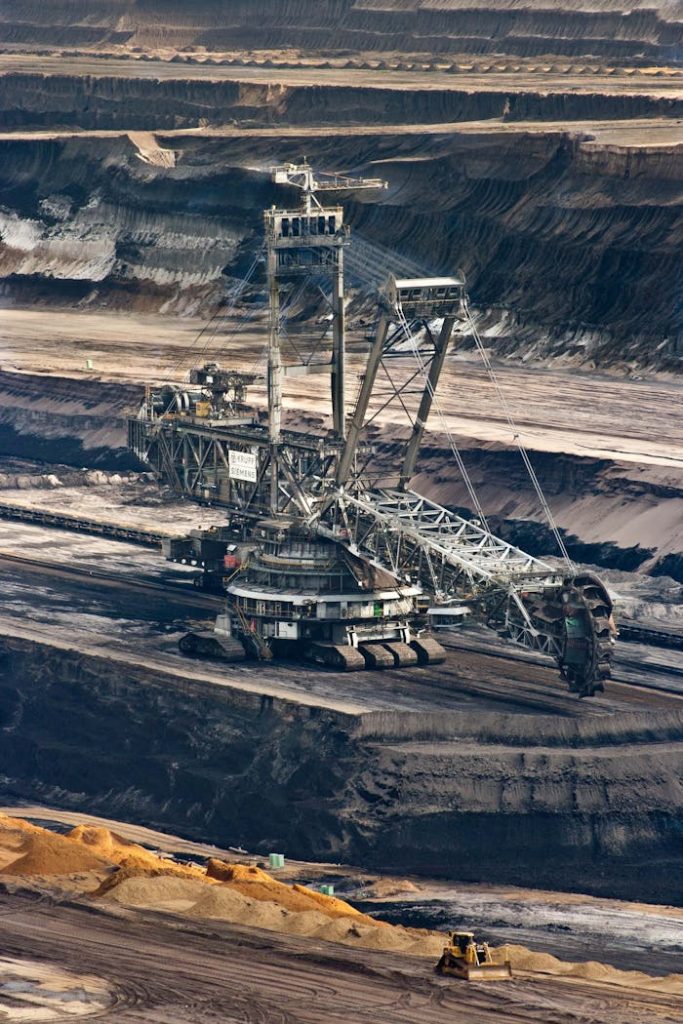 Large bucket wheel excavator operating in an open-pit mine with layered soil and coal.